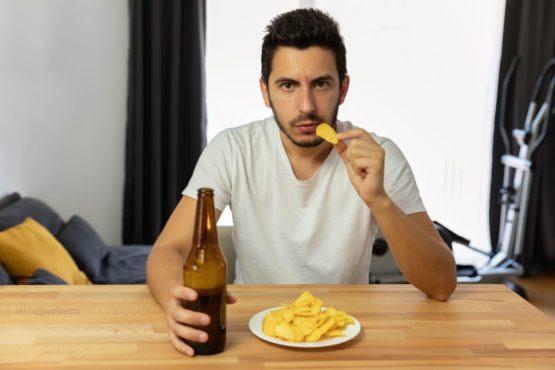 Мужчина пьет пиво, ест чипсы